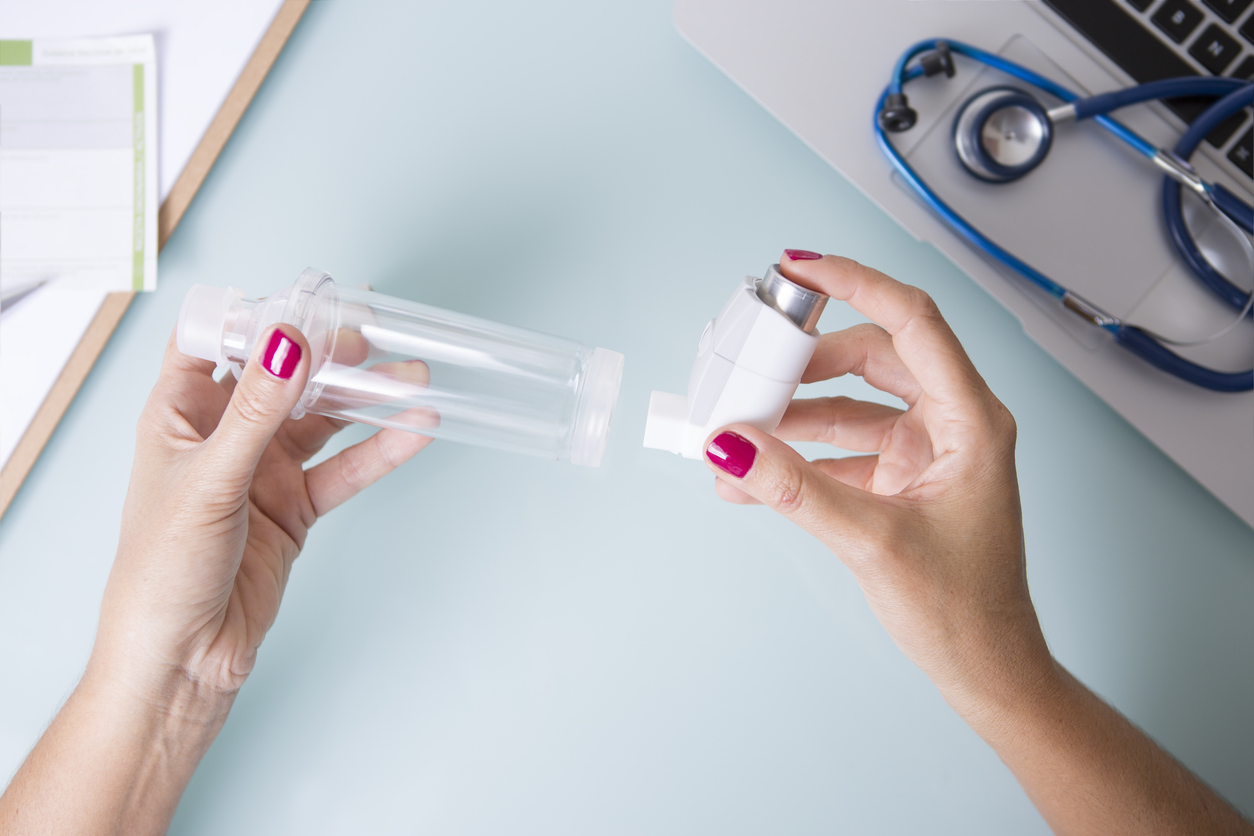 Une personne tient une chambre d'inhalation dans une main et un inhalateur dans l'autre main.